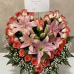 Arreglo floral en forma de corazón con lirios rosados y rosas rojas y blancas, decorado con gypsophila y follaje verde, con tarjeta en la parte superior