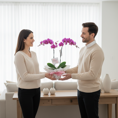 Hombre y mujer de pie frente a frente sosteniendo juntos una maceta de orquídeas rosas sobre una mesa de madera en un salón blanco y luminoso