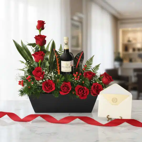 Arreglo floral CINZIA con 12 rosas rojas, follaje verde, bayas rojas y una botella de vino tinto, presentado en una base negr