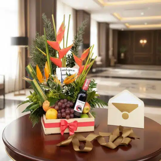Arreglo floral exótico con flores de ave del paraíso y heliconias, piñas, uvas, manzanas y naranjas, acompañado de una botell