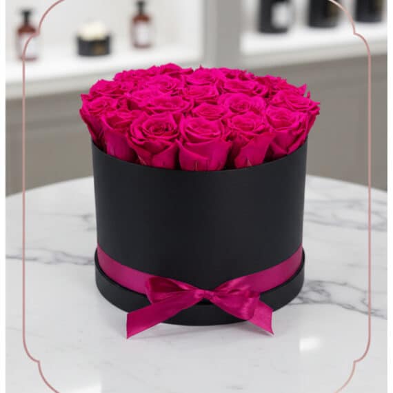 Arreglo Floral Marena: Rosas Fucsia Vibrantes en Caja Negra Elegante Arreglo Floral Marena con 21 rosas fucsia vibrantes y frescas en una caja redonda negra con lazo fucsia, sobre una mesa de má