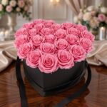 Arreglo Floral Perla con 24 rosas rosadas vibrantes en una caja negra en forma de corazón, sobre una mesa de madera pulida en