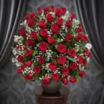 Impresionante arreglo floral de rosas rojas frescas y gypsophila en un jarrón gris sobre una mesa de madera, con un fondo ele