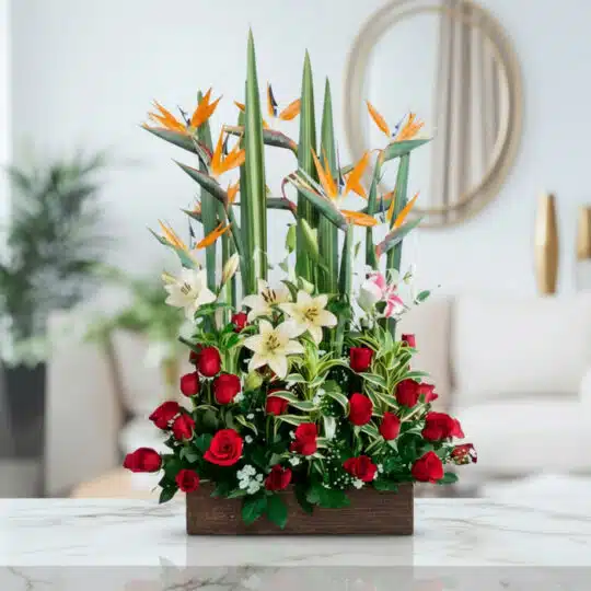 Arreglo floral 'Siempre Juntos' con aves del paraíso, lirios blancos y rosas rojas en base de madera, sobre mármol.