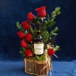 Arreglo floral VERITA con rosas rojas frescas y una botella de vino tinto, presentado en una base de madera rústica, ideal pa