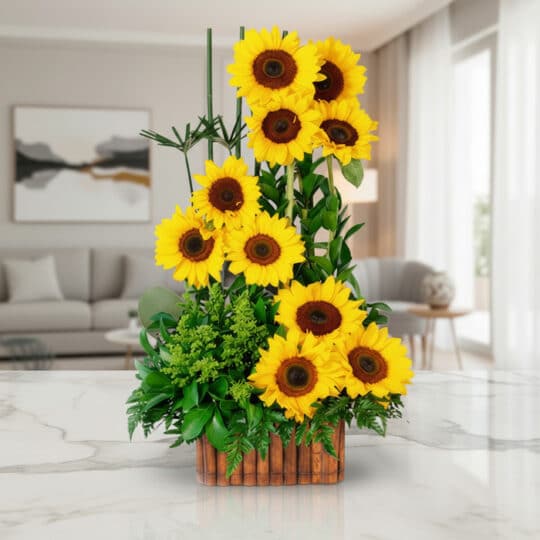Arreglo floral con girasoles vibrantes y follaje verde en una base de madera, sobre una superficie de mármol pulido en un ent