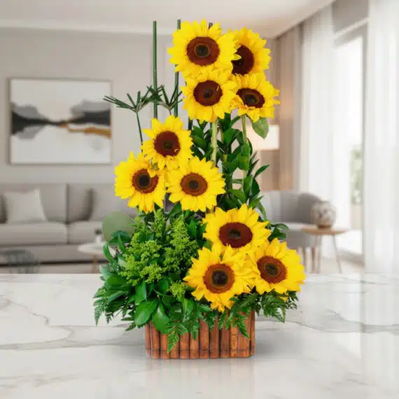Arreglo floral con girasoles vibrantes y follaje verde en una base de madera, sobre una superficie de mármol pulido en un ent