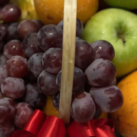 Primer plano extremo de uvas rojas frescas con gotas de rocío, parte de una canasta de frutas premium, con una manzana verde