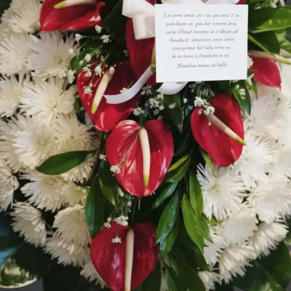 Detalle macro de la Corona Fúnebre Trinidad con anthuriums rojos vibrantes, crisantemos blancos puros y follaje verde, con ro