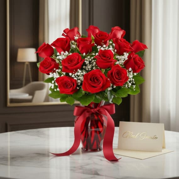 Jarrón Amor Incondicional con un exuberante ramo de rosas rojas frescas y follaje verde, sobre una mesa de mármol en un entor