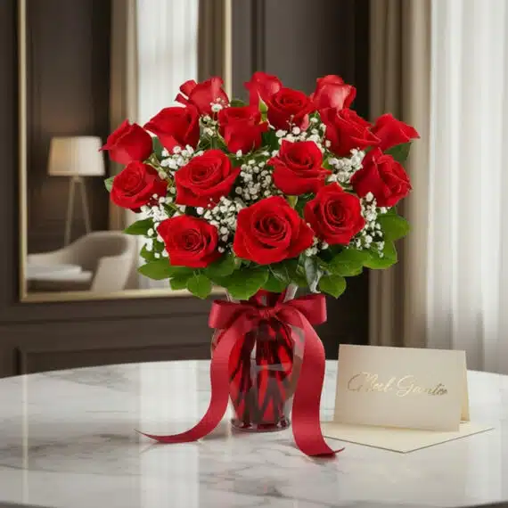 Jarrón Amor Incondicional con un exuberante ramo de rosas rojas frescas y follaje verde, sobre una mesa de mármol en un entor